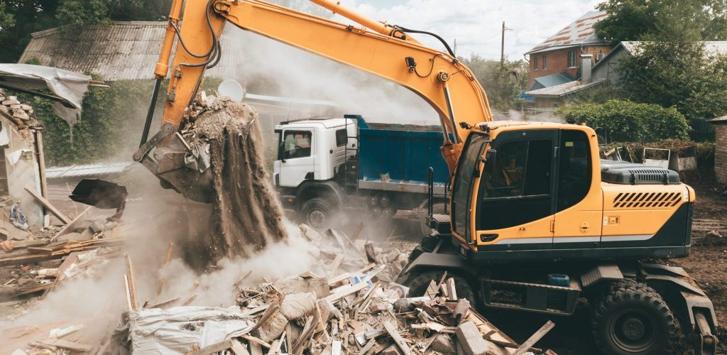 Excavator loads construction waste into truck for removal. Demolition of house. Building destruction. Cleaning up areas for development and new buildings.